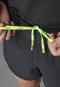 Zwarte sportshorts met een gestructureerd oppervlak, voorzien van felgele koordjes met het label "ADIZERO" en een zijzak.