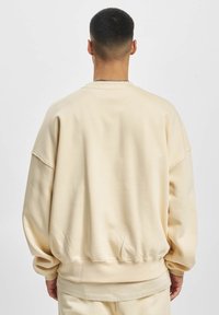 Felpa di colore crema con vestibilità rilassata, polsini e orlo a coste. Texture morbida con spalle scese e dettagli delle cuciture minimi.