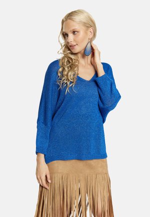 Blauwe, gestructureerde trui met een V-hals en een losse fit, gecombineerd met een lichtbruine suède rok met franjes.