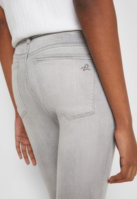 Harmaan denim-farkut, joissa on takataskut, hienovarainen ompelu ja kapea malli, esiteltynä yhdessä tekstuuritetun valkoisen topin kanssa.