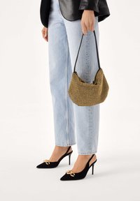 Černá a zlatá texturovaná kabelka s zakřiveným tvarem, nesená černým páskem. Kombinována se světle modrými džíny se širokými nohavicemi a černými sandály na podpatku se zadním popruhem.