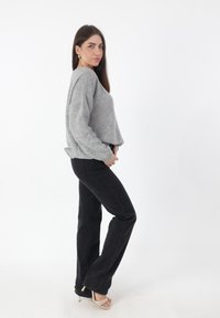 Maglione grigio dalla texture strutturata con maniche ampie, abbinato a jeans neri svasati. Il modello indossa tacchi beige con cinturini su sfondo bianco.