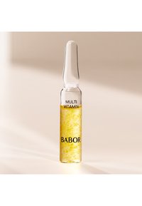 Klar glasampull som innehåller gul vätska, märkt "MULTI VITAMIN" och "BABOR", med en avsmalnande topp och en slät yta.