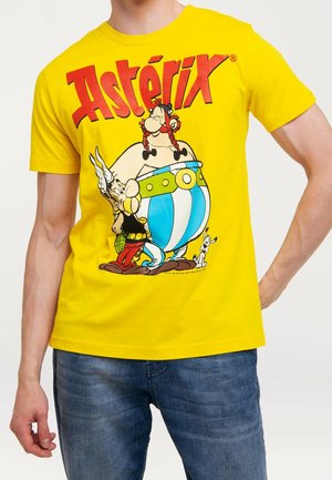 Yellow T-shirt with red "Astérix" text and cartoon characters Astérix, Obélix, and dog standing together.