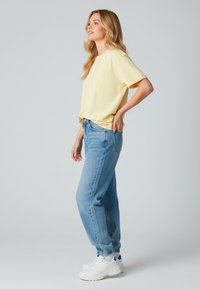 T-shirt gialla a maniche corte abbinata a jeans azzurri chiari e sneakers bianche. I jeans hanno una vestibilità comoda, con polsini a coste alla caviglia.