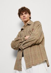 Brown and cream checkered shirt with button front and long sleeves. Soft texture with a relaxed fit, featuring subtle red and blue accents.