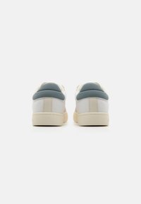 White sneakers with a soft fabric design, blue accents on the heel, and a cream rubber sole, featuring a simple and clean aesthetic.