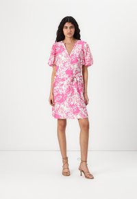 Rochie scurtă cu mâneci scurte, puffed, de culoare roz cu un model floral alb, decolteu în V, talie marcată printr-o curea și tiv până la genunchi. Asortată cu sandale bej cu curele.