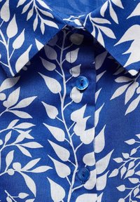 Camicia di cotone blu con motivo a foglia bianca, colletto classico e un bottone blu sul davanti. Il tessuto appare liscio e leggero.