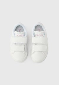 Chaussures blanches Lacoste avec deux bandes auto-agrippantes, bout arrondi et semelles intérieures texturées. Design minimaliste avec un logo sur le talon et à l'intérieur.