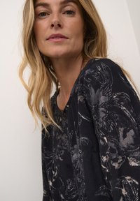 Marinebluse mit floralen Musterungen in Grautönen, Rundhalsausschnitt mit einem dekorativen Knopf und lässigen langen Ärmeln. Weicher Stoff.
