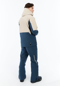 Blauwe en beige herenjas met een capuchon, contrasterende kleuren en een ritszak op de broek. Soepele textuur, gemaakt voor winterkleding.
