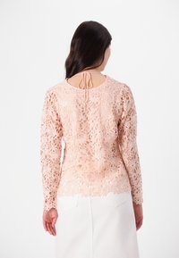 Spitzenoberteil mit langen Ärmeln in sanftem Pfirsich, verziert mit Blumenmustern, transparenten Abschnitten und einer Schleifenbinde im Rücken. Glatte Textur mit filigranen Designs.