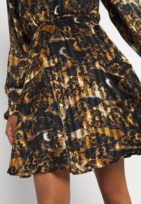 Jupe fluide avec une taille élastique et des manches longues, avec un motif abstrait floral et à rayures marron, noir et beige.