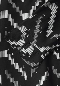 Tessuto nero con un motivo geometrico bianco. Primo piano di un polsino di camicia con pieghe e disegni lineari a contrasto. Texture morbida.
