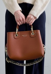 Sac à main en cuir marron avec quincaillerie dorée, poignées doubles et une bandoulière ajustable à motif. Texture lisse avec un design structuré.