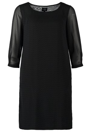 Vestido negro con mangas transparentes, cuello redondo y tejido texturizado. Combinado con botas de tobillo grises y un pequeño bolso bandolera.