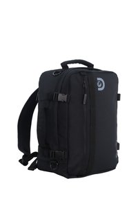 Mochila negra de forma rectangular, hecha de tejido duradero. Cuenta con tirantes ajustables, un asa superior, un bolsillo frontal y detalles con el logotipo.