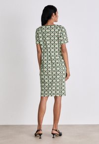 Kurzärmliges, figurbetontes Kleid in Grün mit einem geometrischen Blumenmuster. Glatter Stoff, knieumspielend, mit rundem Ausschnitt und seitlichen Schlitzen.