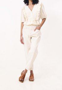 Ljust färgad, volangblus med V-ringning, matchad med krämfärgade byxor och bruna klackslip-ins; mjuka texturer och avslappnad passform.