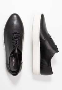 Zapatos de cuero negro con cordones, punta redonda, suela de goma blanca y diseño minimalista. Textura suave con detalles de costura sutiles.