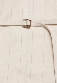 Tissu beige à fines rayures verticales avec une ceinture assortie passée à travers une petite boucle carrée en métal doré.