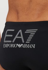 Schwarze Schwimmshorts mit dem silbernen "EA7 Emporio Armani"-Logo, einem strukturierten Muster und einer engen Passform.