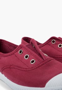 Baskets slip-on en toile bordeaux avec semelles en caoutchouc blanches. Les caractéristiques incluent des œillets en métal et des coutures renforcées le long des coutures.