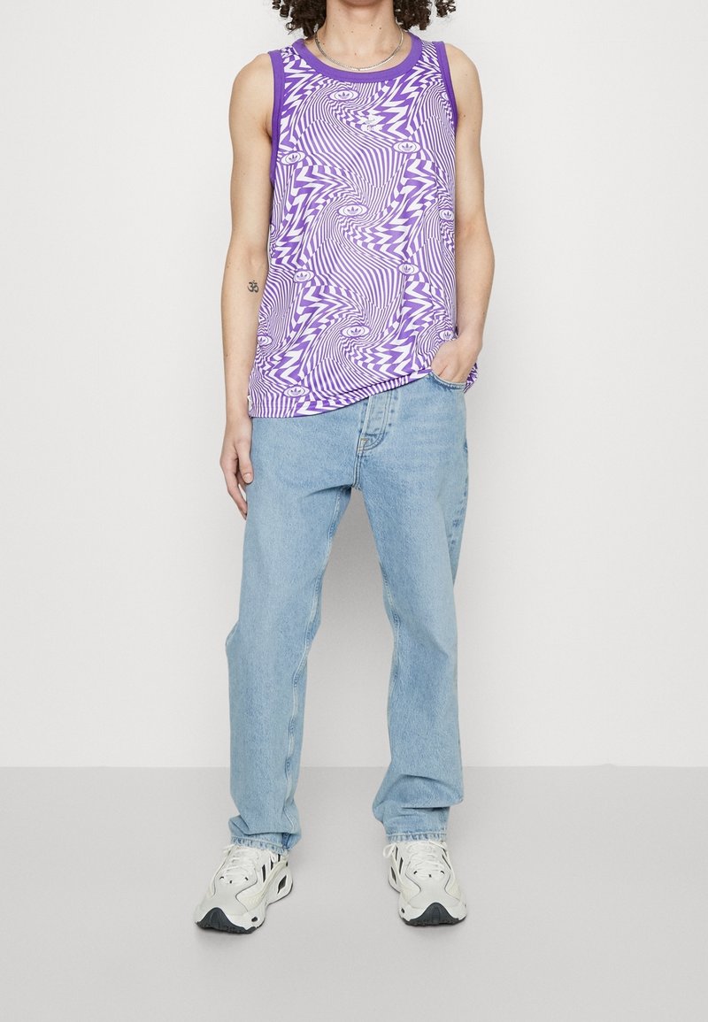 Lila linne med ett virvlande mönster, parat med ljusblå löst sittande jeans. Materialet verkar vara lätt; skorna är vita med svarta detaljer.