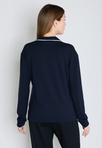 Camisa de manga larga color marino con cuello, que presenta un ribete blanco en el escote y los puños. Tejido suave y liso con un ajuste relajado.