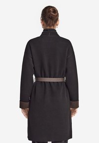 Schwarzer Wollmantel mit hohem Kragen, tailliertem Bund und kontrastierenden braunen Manschetten. Verfügt über eine lockere Passform und ein minimalistisches Design.