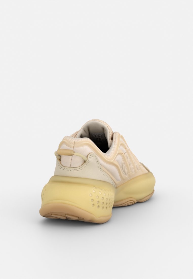 Zapato deportivo beige con una parte superior de cuero liso, acentos texturizados y una suela amarilla semitransparente. Cuenta con una pestaña de tirón en la parte trasera.