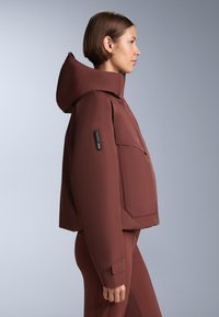 Rjava podložena jakna z visokim ovratnikom in kapuco, z žepom na zadrgo na rokavu in prilegajočim zapiranjem na zapestju, gladka tekstura.