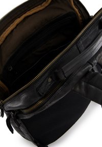 Czarna skórzana torba z złotym zamkiem, z brązowym materiałowym wykończeniem, wieloma kieszeniami wewnętrznymi oraz teksturowanym czarnym siatkowym dnem.