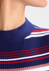 Maglione a coste con collo alto, caratterizzato da righe orizzontali in blu navy, rosso, bianco e rosa pallido. Morbido al tatto con un contrasto di colori dettagliato.