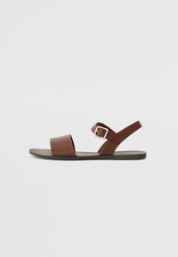 Brune lær sandal med en bred forretningsrem, justerbar spænde ankelrem og flad gummisål. Minimalistisk design og glat tekstur.