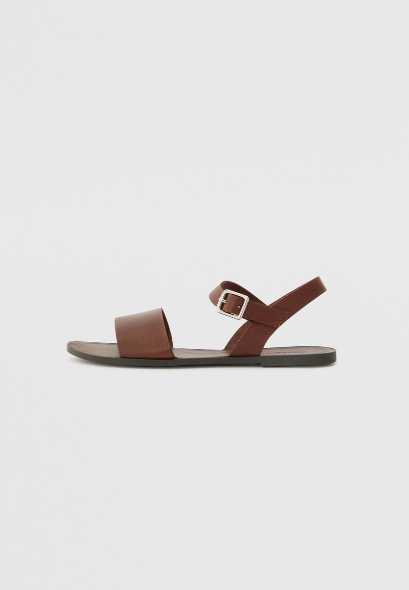 Brune lær sandal med en bred forretningsrem, justerbar spænde ankelrem og flad gummisål. Minimalistisk design og glat tekstur.