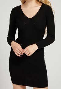 Robe noire en maille côtelée avec manches longues et décolleté en V, présentant une silhouette ajustée et une texture lisse.