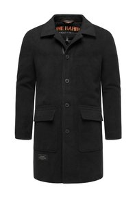 Fekete gyapjúpulóver gombos elejével, hegyes gallérral, két elülső zsebbel és márkázott folttal az alsó bal oldalon.