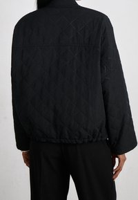 Zwarte gewatteerde jas met een relaxte pasvorm, voorzien van een ronde kraag, elastische zoom en een diamantpatroon over de stof.