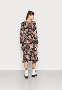Vestido floral com um fundo escuro, mangas longas, bainha com babados e detalhe na parte de trás em forma de chave. Combinado com botas brancas até o tornozelo e solas grossas.