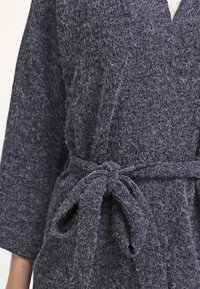 Stickad morgonrock i mörkgrått, med en mjuk, texturerad yta, vid ärmar och midja med bälte som är knutet prydligt.