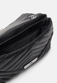 Black quilted faux leather bag with a shiny silver hardware accent. Features an open top and interior logo pattern.