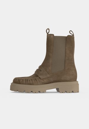 Bottine Chelsea en daim marron avec semelle épaisse crantée, panneaux latéraux élastiques, languettes en haut, et détail de couture style mocassin sur le bout.