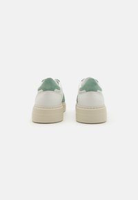 Grüne und weiße Sneaker mit gepolstertem Fersenbereich und strukturierten Akzenten. Verfügt über eine dicke beigen Sohle mit Logo-Detail auf der Rückseite.