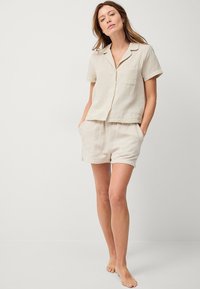 Beige katoenen loungewear set met een kortomtop met knopen en een zak, en bijpassende shorts met drawstring in een ontspannen pasvorm.