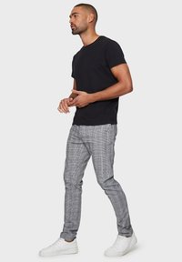 Schwarzes Baumwoll-T-Shirt, kombiniert mit grauen karierten Hosen und weißen Sneakers, in schlanker Passform und mit subtilen Texturen im Stoff.