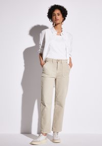 Béžové bavlněné kalhoty s uvolněným střihem a předními kapsami, doplněné bílým tílkem a rozepnutou bílou košilí. Texturovaná látka.