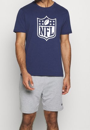 Homme portant un t-shirt bleu marine avec un logo NFL blanc et un short de sport gris clair avec un petit swoosh Nike noir.