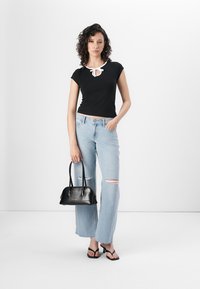 Juodas trumpas rankovėmis marškinėliai su balta apykaklės detale, šviesiai mėlyni suplėšyti džinsai ir juoda rankinė. Modelis dėvi juodus šlepetes.